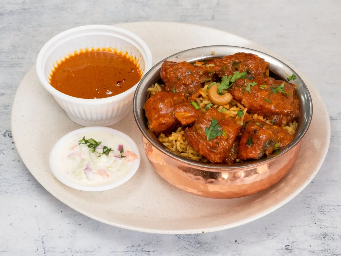 Fish briyani served in a hammered copper handi with curry gravy and raita
