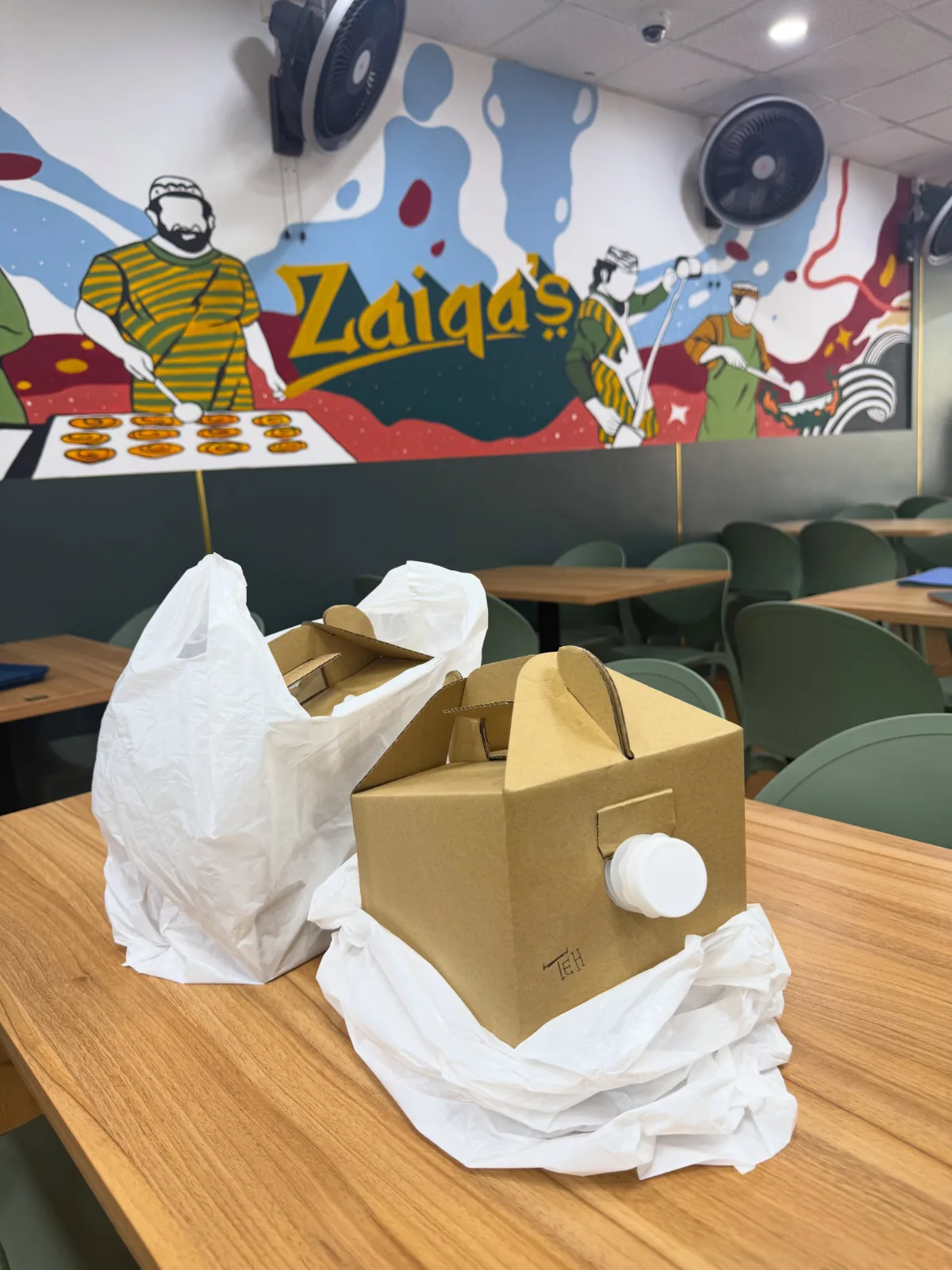 The mural inside Zaiqa’s Cafe — an illustrated wall with “Zaiqa’s” in gold script at its centre, above the indoor dining room