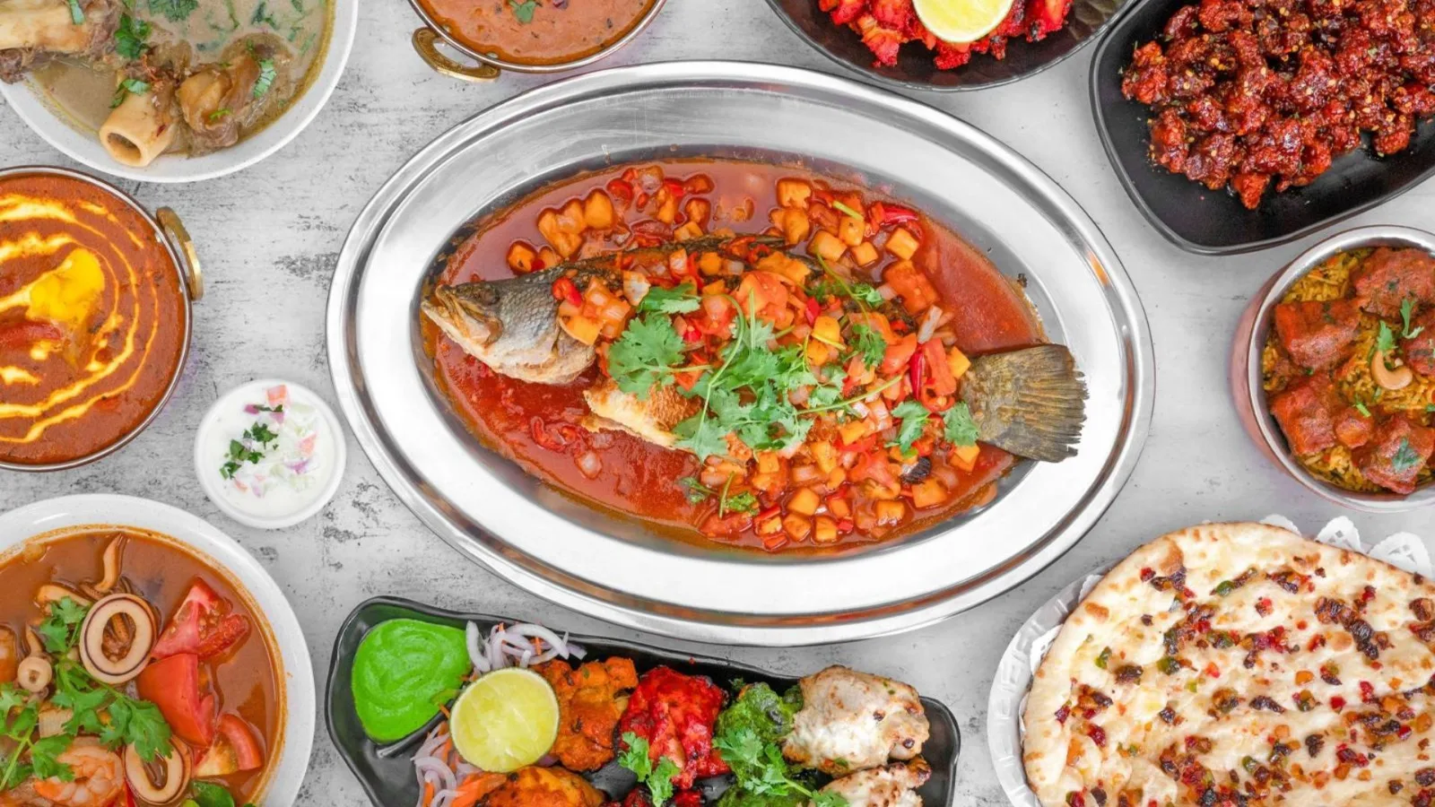 Whole fried fish in Thai-style tomato-chilli sauce on a steel platter, with curries, naan and a tandoori platter around it